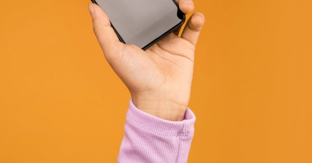 Close-up of a hand holding a smartphone against an orange background.