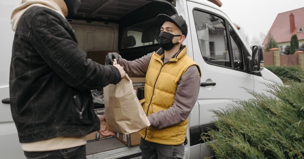Two men wearing face masks exchange a package by a delivery van outdoors.