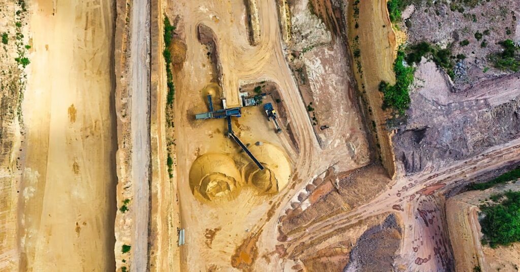 An aerial shot of an open-pit mine with machinery and pathways visible, surrounded by landscape.