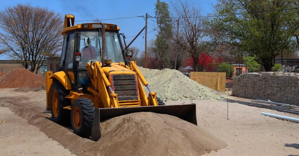 A yellow backhoe loader at a construction site moving sand on a clear day.