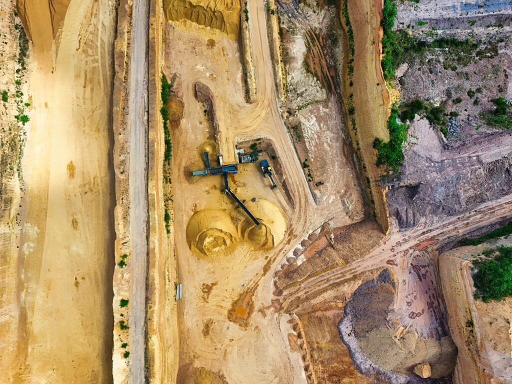 An aerial shot of an open-pit mine with machinery and pathways visible, surrounded by landscape.